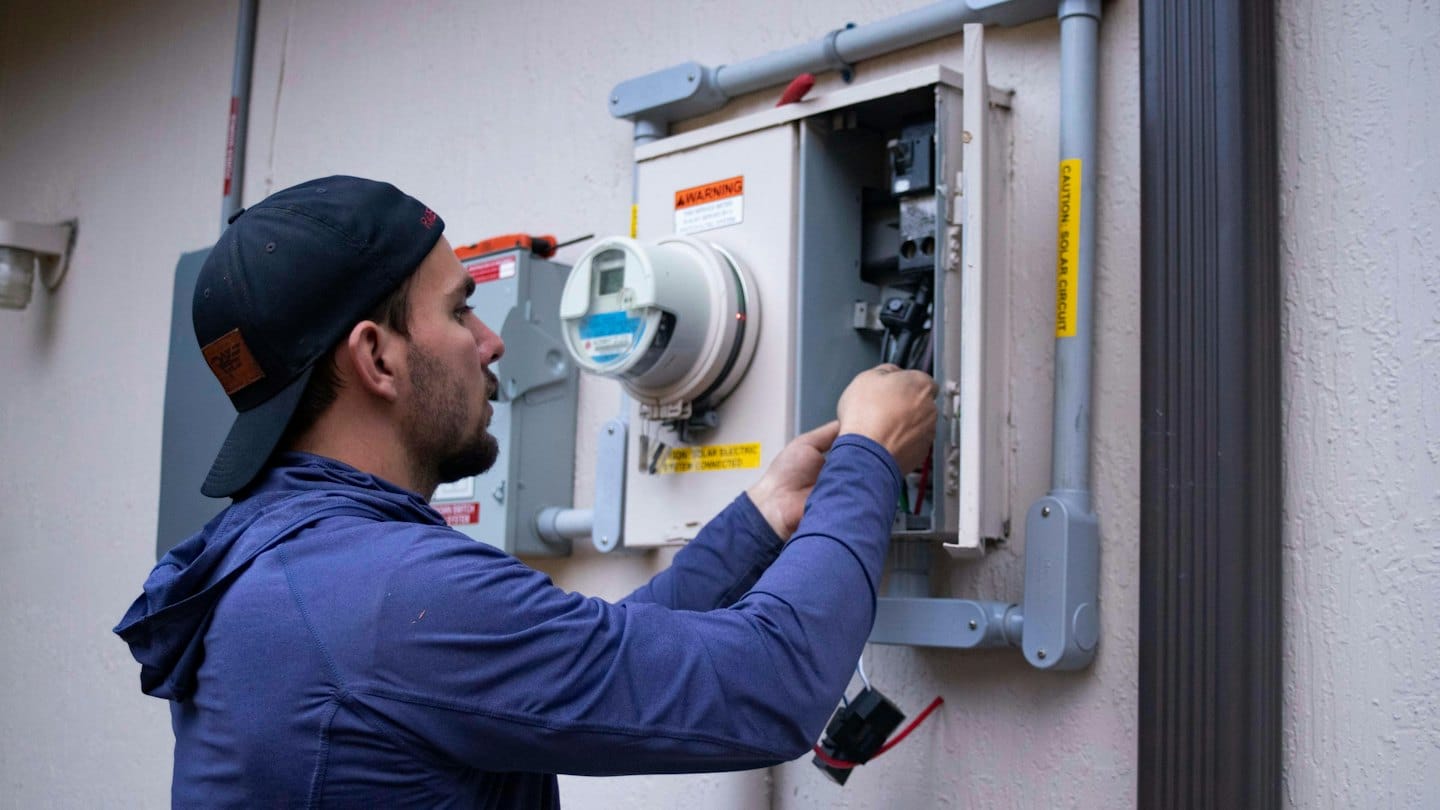 Technician connecting wires in an outdoor electrical panel.