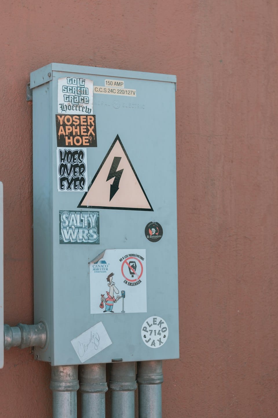 Weathered utility box covered in stickers on a stucco wall.