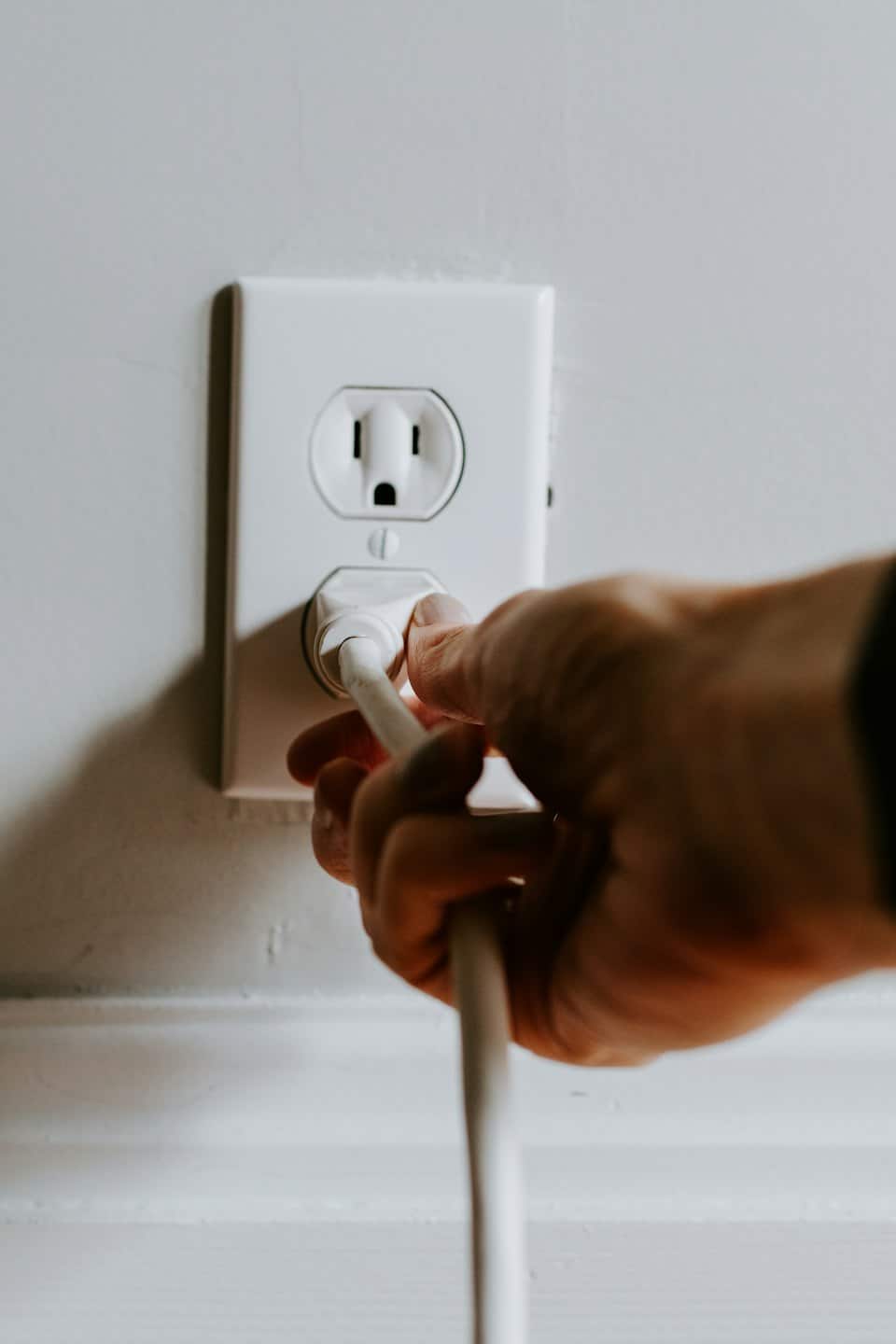 Hand plugging a white cord into a wall outlet.