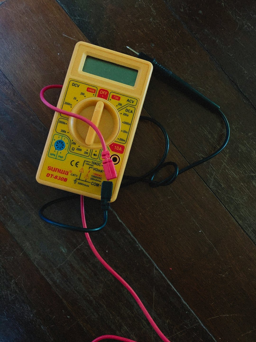 Yellow multimeter with red and black probes on wooden floor.